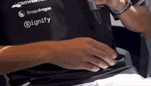 a person wearing a black shirt with snapdragon and signify logos on it