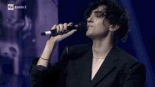 a man with curly hair is singing into a microphone while wearing a black jacket .