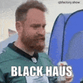 a man with a beard is holding a can of beer and wearing a green jersey that says black haus