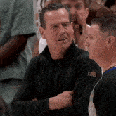 a man wearing a black cavs shirt talks to another man