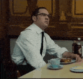 a man wearing glasses sits at a table with a plate of food