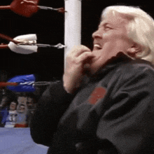 a man in a black jacket is standing in a boxing ring eating something