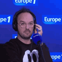 a man wearing headphones and glasses is talking into a microphone in front of a blue background .