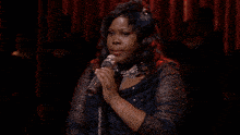 a woman singing into a silver microphone with a feather in her hair