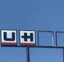 a large billboard with the letters u and h on it is hanging from a pole .