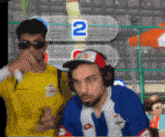 two men are playing a video game with the number 2 on the screen behind them