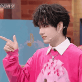 a young man wearing a pink sweater and a white shirt is pointing