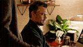 a man with a beard is sitting at a desk with a plant in the background