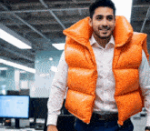 a man wearing an orange vest stands in front of a computer