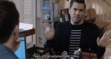 a man in a black and white striped shirt is talking to another man in a room .