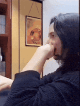 a man covering his mouth with his hand in front of a framed picture