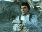 a man wearing a silver jacket and gloves is holding a watch that says " ii " on it