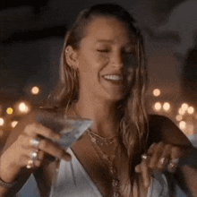 a woman in a white top is holding a martini glass and smiling .