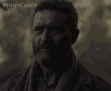 a man with a beard and a scarf looks at the camera with #highcastle written below him