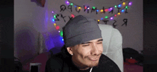 a man wearing a gray beanie is sitting in front of a wall with the letters t and t on it