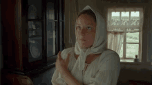 a woman wearing a white scarf around her head is standing in front of a window