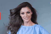 a woman wearing a blue shirt is smiling with her hair blowing in the wind