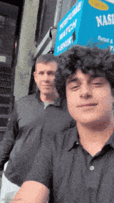 two men are posing for a picture in front of a perfume watch t-shirt store