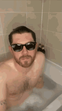 a shirtless man wearing sunglasses is taking a bath in a bathtub