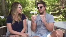 a man and a woman are sitting on a couch and the man is wearing sunglasses and a shirt that says college