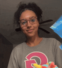 a woman wearing glasses and a grey shirt with a pink letter g on it