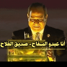 a man in a suit and tie stands behind a podium with arabic writing behind him