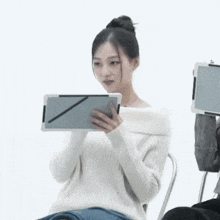 a woman in a white sweater is holding a tablet in her hand