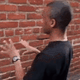 a man is pointing at a brick wall while wearing a watch .