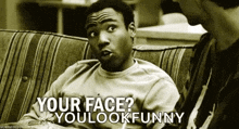 a man is sitting on a couch talking to another man and says " your face you look funny " .