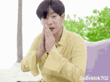a man wearing a yellow shirt is sitting on a purple couch with his hands folded