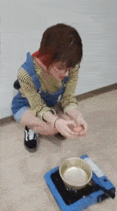 a woman is kneeling down next to a pot on a blue stove