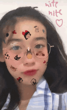 a girl wearing glasses has stickers on her face and the words kite nite written on the wall behind her