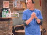 a man in a blue shirt is standing in front of a sign that says please keep your clothes on while doing laundry