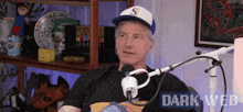 a man wearing a hat is sitting in front of a microphone with the words dark web on the bottom right