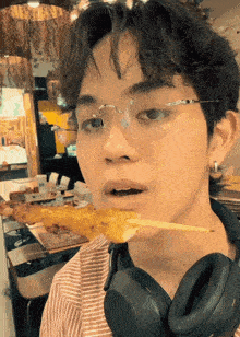 a young man wearing glasses and headphones eating a skewer of food