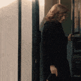 a woman in a black coat is holding a purse and opening a door