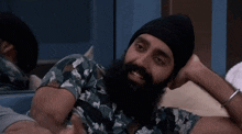 a man with a beard and a beanie is laying on a bed with his head on his hand .