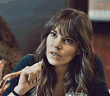 a woman with long hair and bangs is sitting at a table with a glass of wine