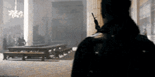 a man holding a gun standing in a room with tables and benches