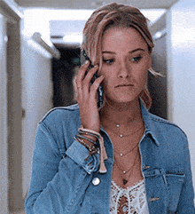 a woman in a blue denim jacket is talking on a cell phone .