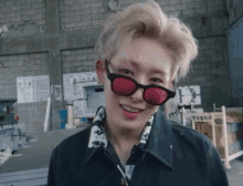 a young man wearing red sunglasses and a black jacket is smiling