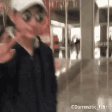 a man wearing sunglasses and a hat is talking on a cell phone in a mall