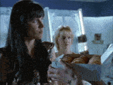 a woman is holding a box of donuts and another woman is standing behind her