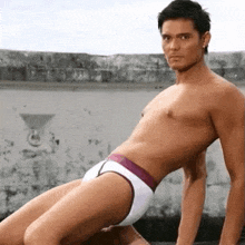 a shirtless man in a white underwear is sitting on a wall .