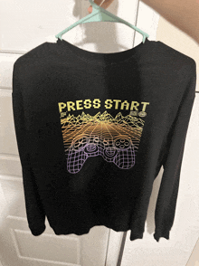 a black shirt that says press start is hanging on a green hanger