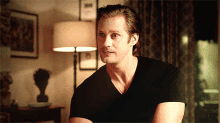 a man in a black shirt is sitting in front of a lamp in a living room