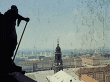 a statue of a man standing on a ledge overlooking a city