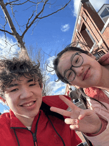 a boy in a red jacket and a girl in glasses pose for a photo