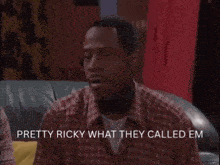 a man in a plaid shirt is sitting on a couch and says " pretty ricky what they called em "