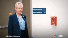 a woman in a suit stands in front of a sign that says emergency department